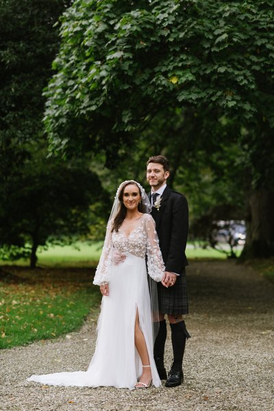 Bride and groom stand in garden park hand in hand holding hands