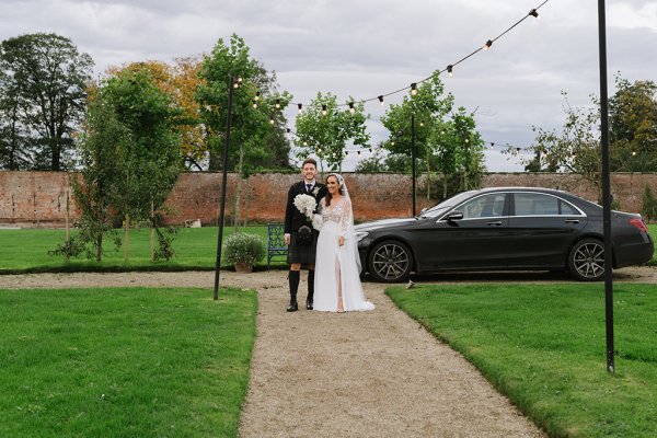 Bride and groom enter venue walk up pathway together bride is holding flowers