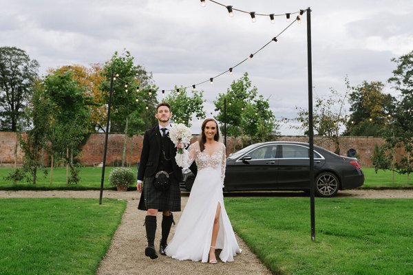 Bride and groom enter venue walk up pathway together bride is holding flowers