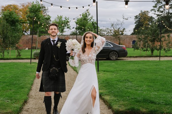 Bride and groom enter venue walk up pathway together bride is holding flowers