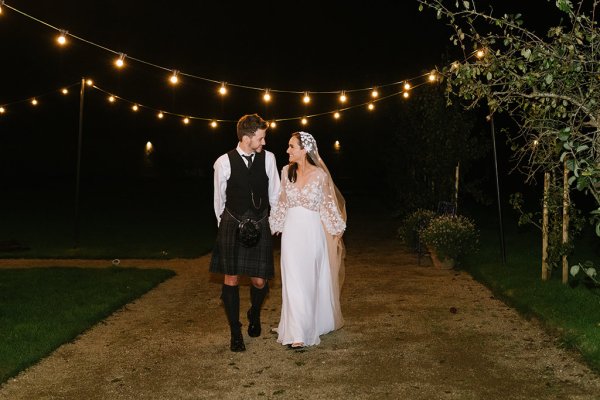 Bride and groom walking at nighttime with lights in background