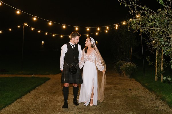 Bride and groom walking at nighttime with lights in background