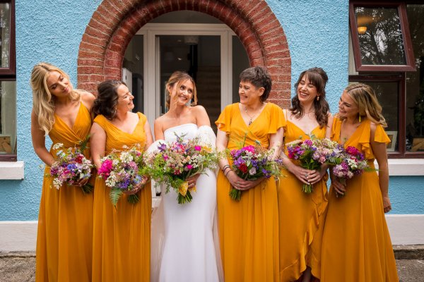 Bride and bridesmaids wearing orange holding bouquet of flowers