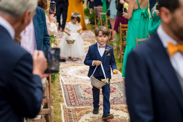 Little boy throws flowers flower girl in background behind him