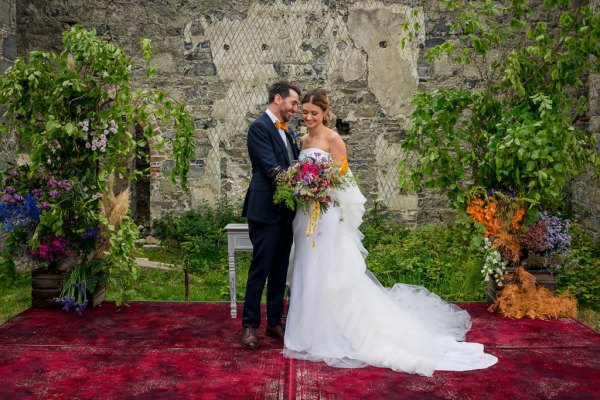 Bride holds bouquet of flowers standing with groom on bed of flowers