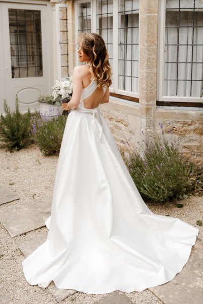 Bride on her own white bridal gown/dress she holds bouquet of flowers train from behind