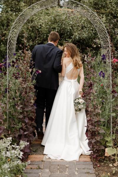 Bride looks over shoulder to camera in garden holding flowers