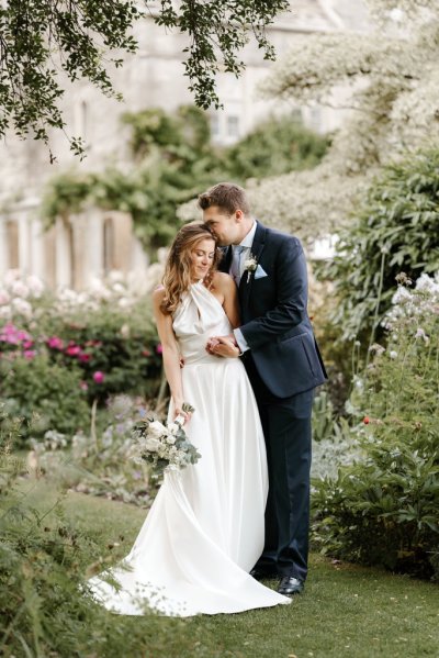 Bride and groom standing in garden holding flowers kiss on head