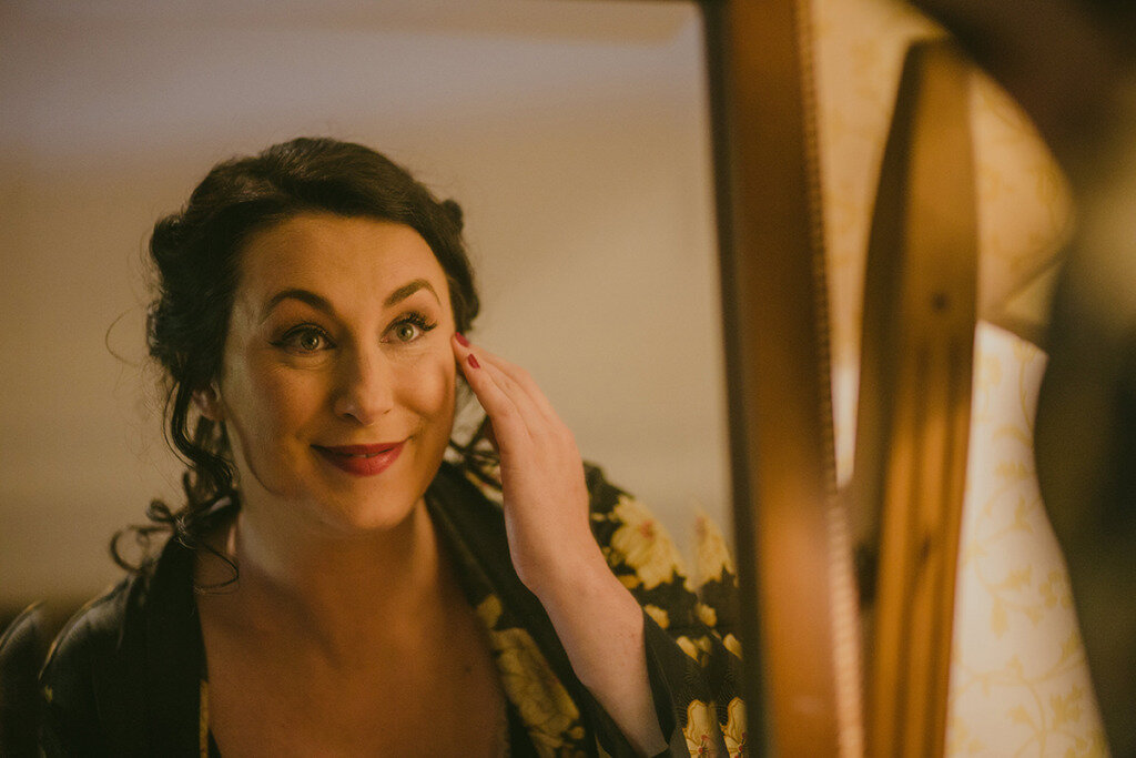 Bride looks in the mirror smiling at makeup