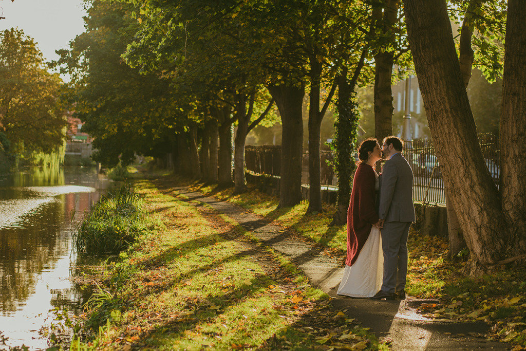 Sun is shining through trees in park canal setting bride and groom