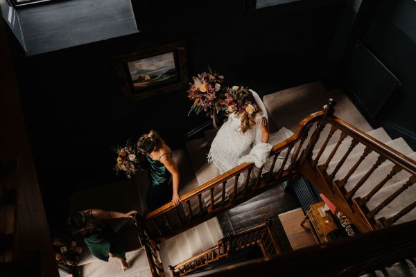 Bride walking down stairs staircase holding flowers and bridesmaid