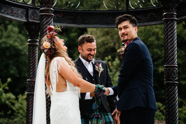 Bride and groom ribbon hands laughing with officiant