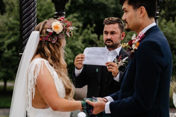 Bride officiant and groom holding hands bound ribbon