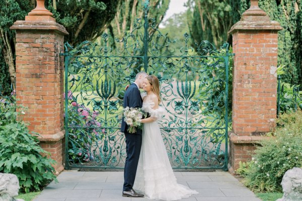 Bride and groom in front of flower gate embracing hugging kissing