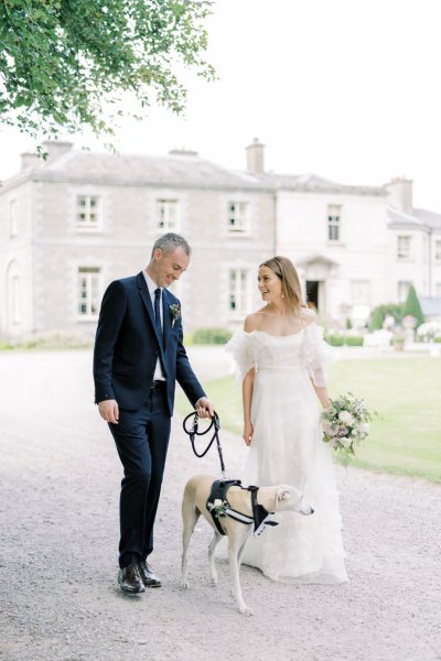 Bride and groom walk with greyhound dog