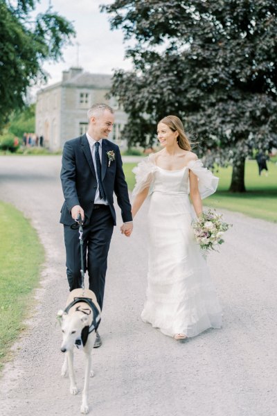 Bride and groom walk with greyhound dog on a leash lead