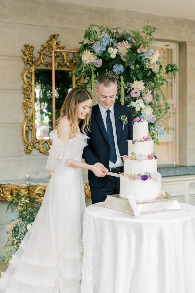 Bride and groom cut the cake mirror and flowers in background