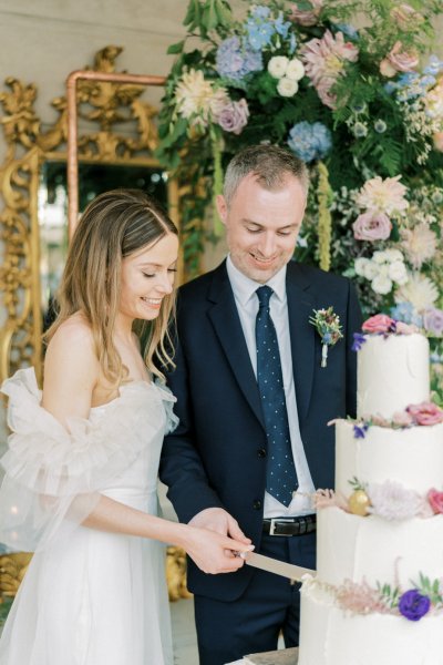 Bride and groom cut the cake mirror and flowers in background