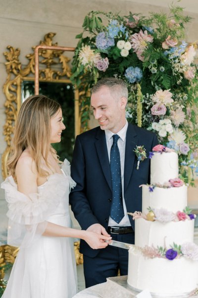 Bride and groom cut the cake mirror and flowers in background