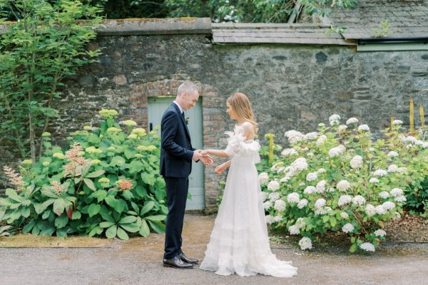 Bride and groom hold hands in garden