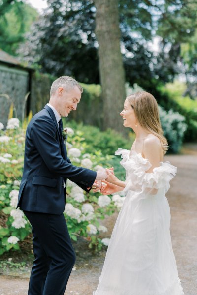 Bride and groom hold hands in garden hug