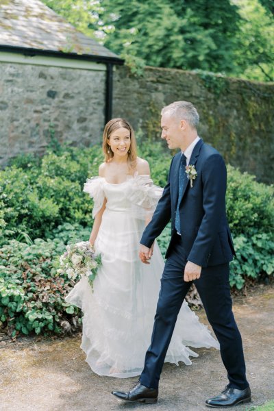 Couple hold hands in garden bride and groom walk