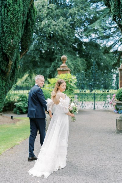 Bride and groom look behind them to camera and they walk in garden