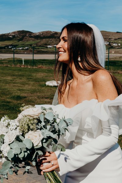 Bride on her own in the sunshine smiling holding bouquet of flowers