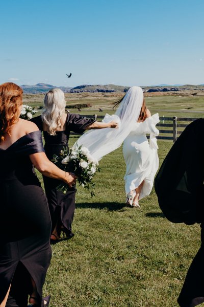 Bride from behind veil blowing in wind and bridesmaids wearing black