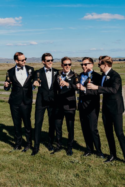 Groom holding bottle of beer with groomsmen on grass exterior