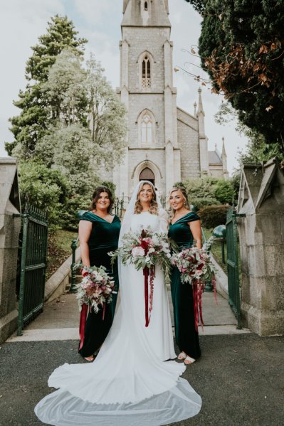 Bride and bridesmaids in front of church/cathedral holding flowers/bouquet