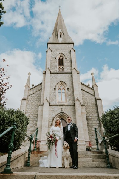 Bride and groom in front of church flowers/bouquet