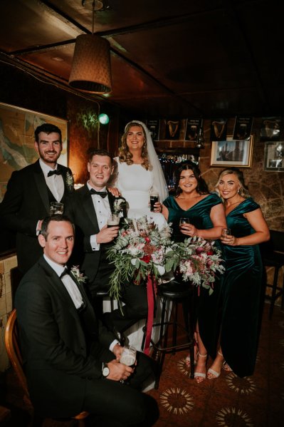 Bride bridesmaids groom and groomsmen holding flowers/bouquet in pub