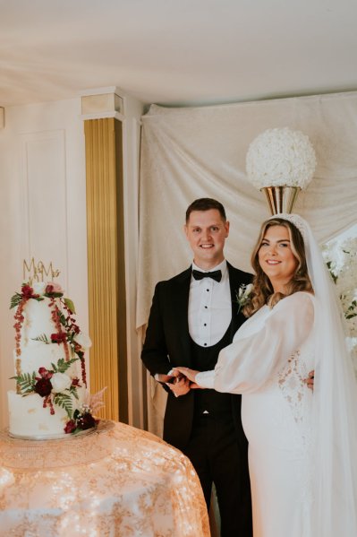 Bride and groom smile in front of wedding cake