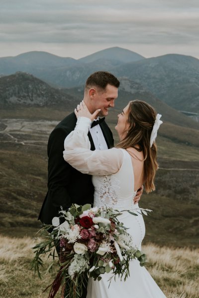 Bride and groom on mountain landscape lake and fog rocks sky view hands on face