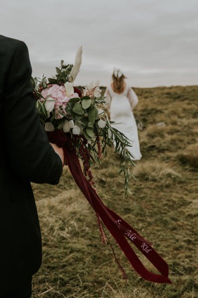 Groom holds flowers/bouquet walking towards bride