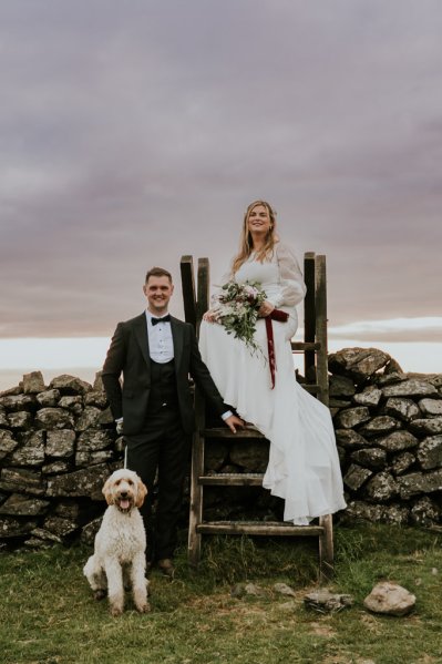 Bride groom and dog sitting on ladder rocks