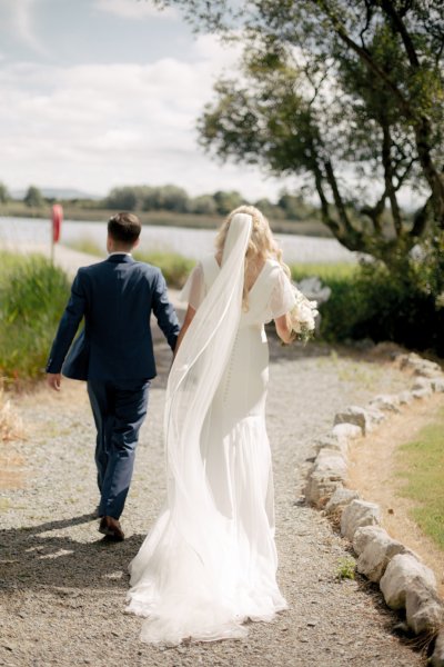 Bride and groom walk through garden on sunny day