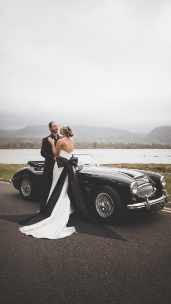 Bride and groom standing hugging beside wedding car