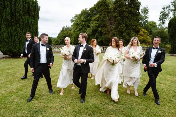 Groom bride groomsmen and bridesmaids walk on grass