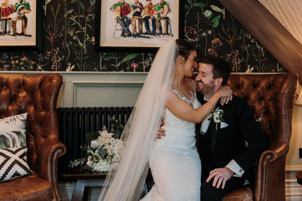 Bride sits on grooms lap smiling interior shot