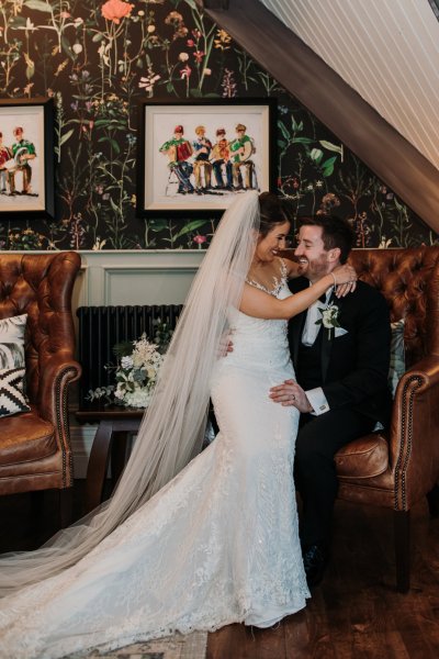 Bride sits on grooms lap smiling interior shot