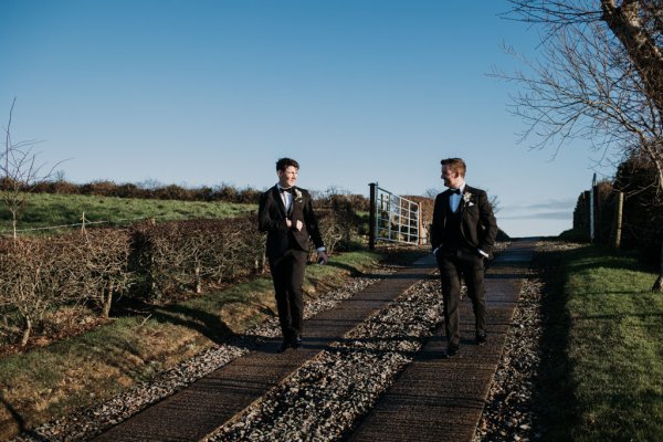 Groom and groomsman walk along farm setting