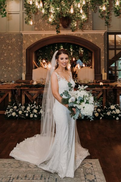 Happy bride holding bouquet of flowers veil and train dress detail