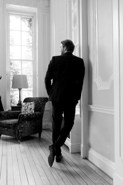 Black and white image of groom leaning against wall