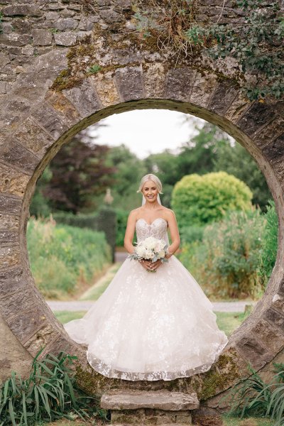 Bride stands in oval-shaped archway garden