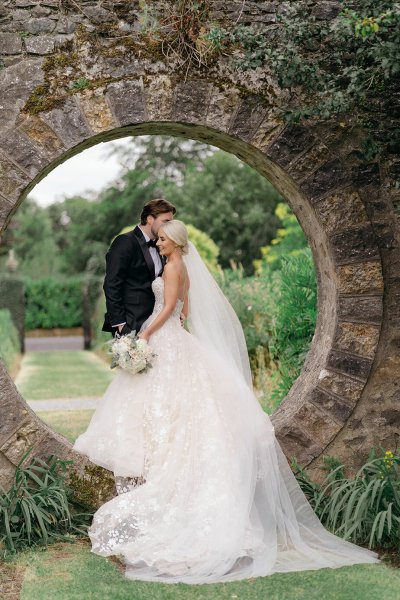 Bride and groom stand in oval-shaped archway garden