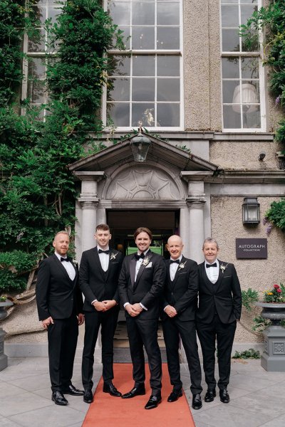 Groom and groomsmen outside venue on red carpet