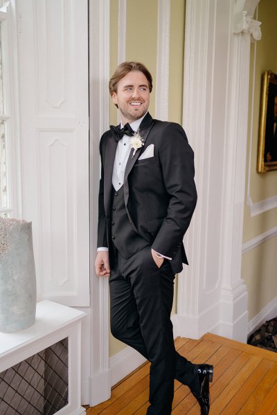 Groom standing in black suit and tie tuxedo