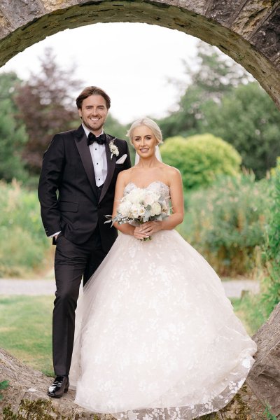 Bride and groom face the camera holding bouquet of flowers